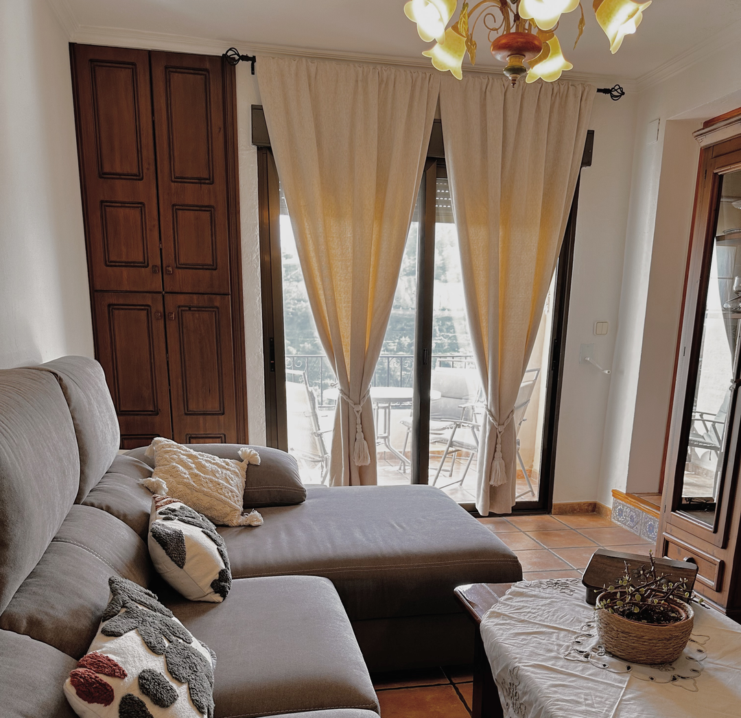 Cozy and well-lit living room featuring a gray sectional sofa and tied-back light-colored floor-to-ceiling curtains.