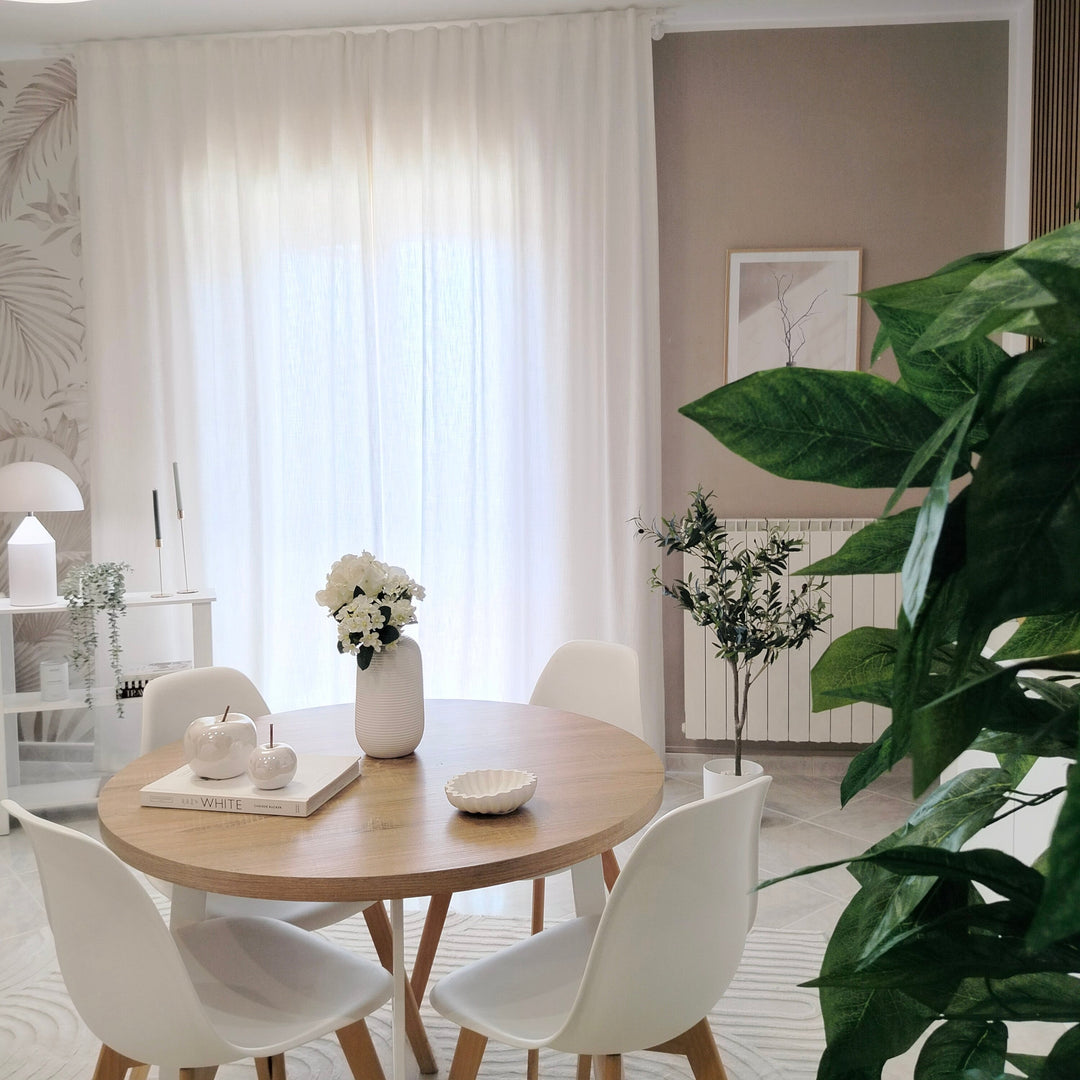 Modern cozy dining space featuring a round wooden table, white chairs, and translucent white sheer curtains.