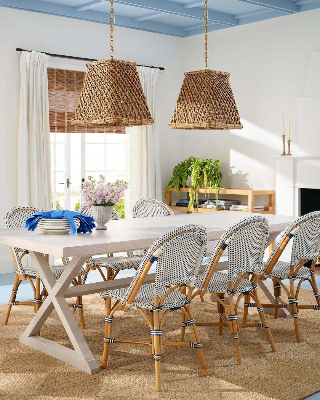 Elegant dining room featuring white window curtains, woven wood shades, a wooden dining table, and pendant lights.