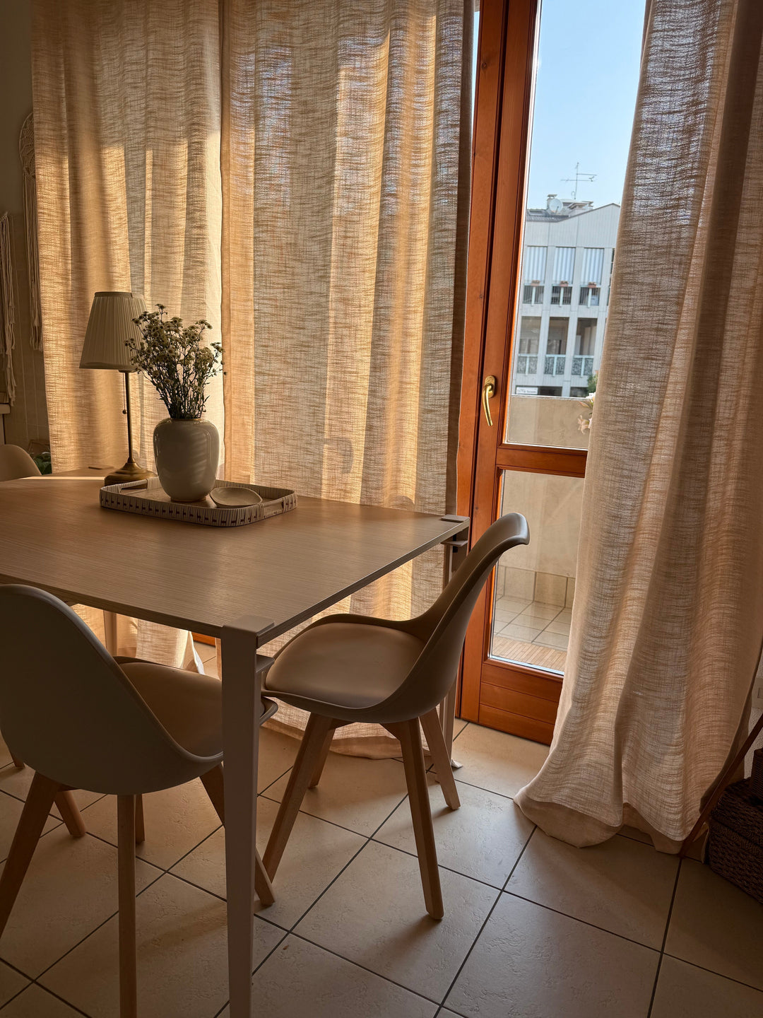 Well-lit cozy dining area with a wooden dining table, modern chairs, and translucent linen curtains.