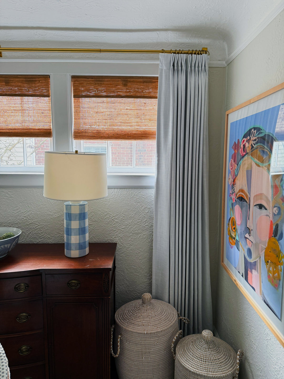 Cozy modern window corner featuring woven blinds, grey pleated curtains, and a table lamp.