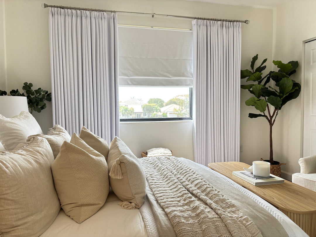 Modern minimalist bedroom featuring white pleated curtains, a Roman shade, and neutral bedding.