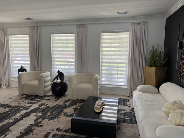 Panorama of a modern living room featuring multiple windows with zebra blinds and elegant floor-to-ceiling curtains.